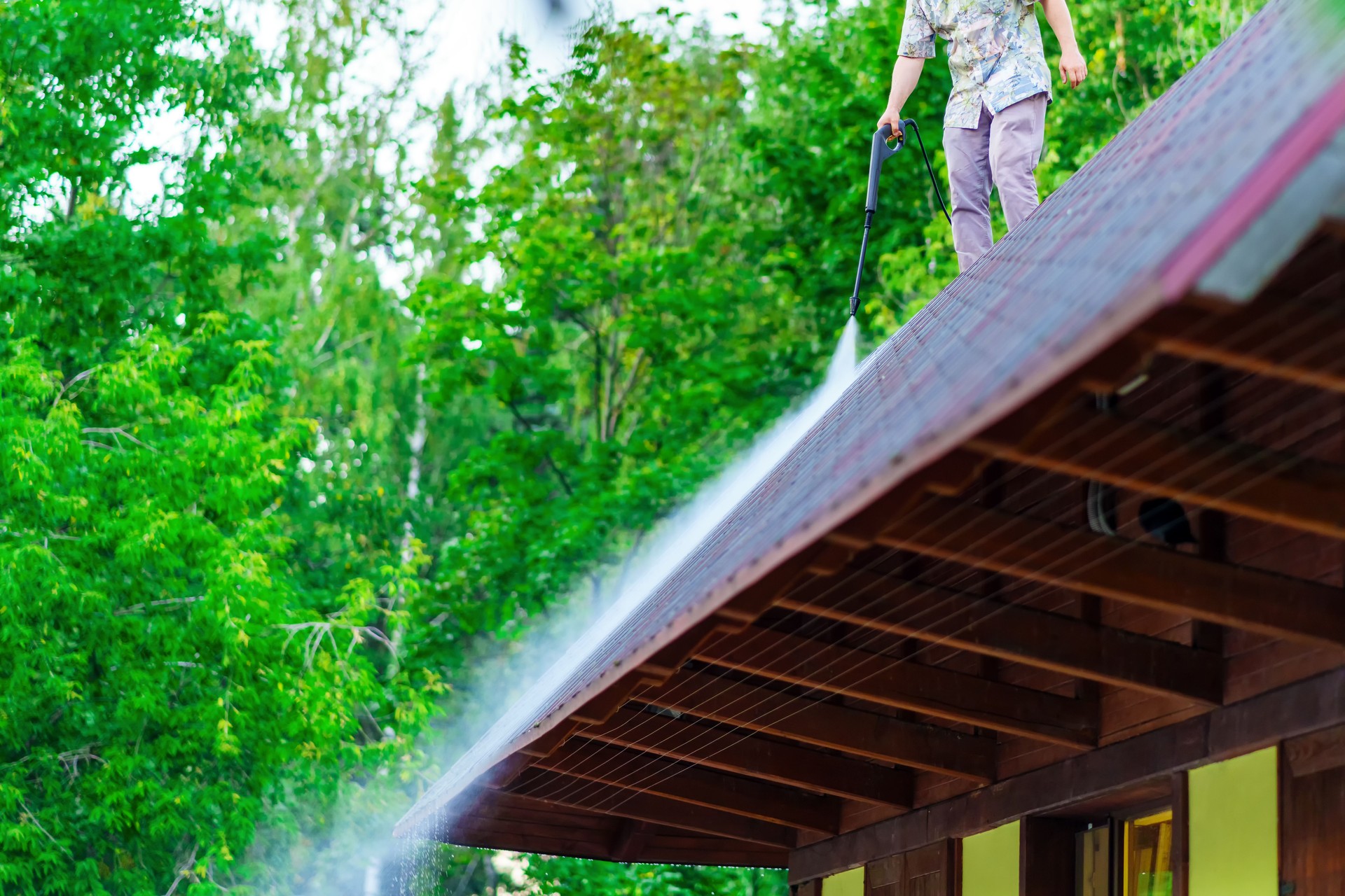 A man washes the roof of a building with a pressure wash